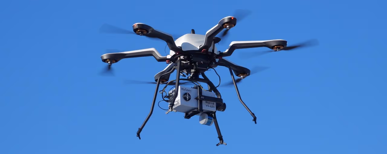 Multi-rotor drone with mounted HySpex imaging sensor flying against a clear blue sky.