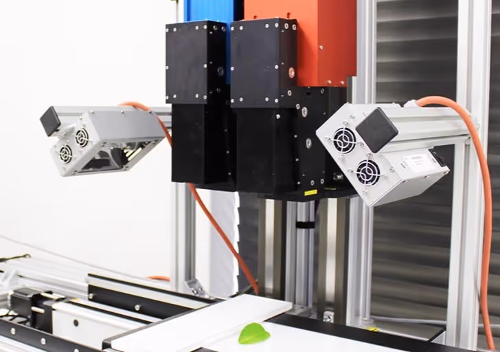 Close-up of a hyperspectral imaging device with dual sensor modules positioned above a single green leaf on a white platform.
