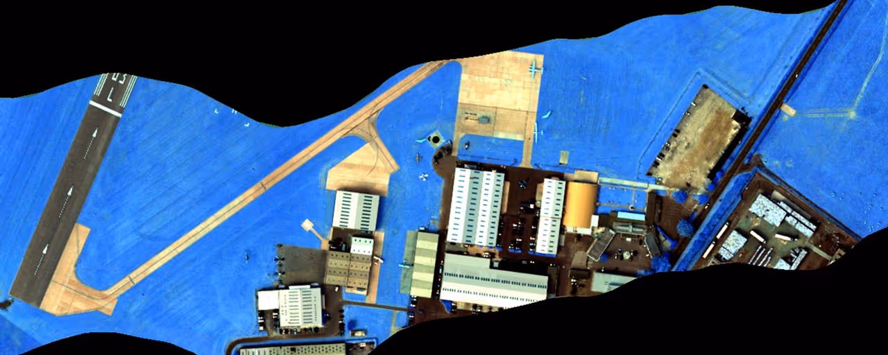 Aerial view of an airport area with buildings, parked airplanes, and a runway, with vegetation rendered in blue.