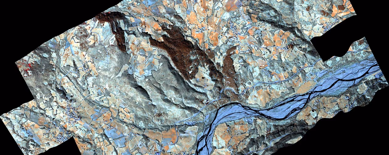 False-color satellite image showing a river meandering through varied terrain with agricultural fields and forested hills.