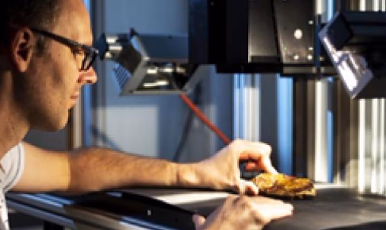 Scientist examining a rock sample under a laboratory scanning device.