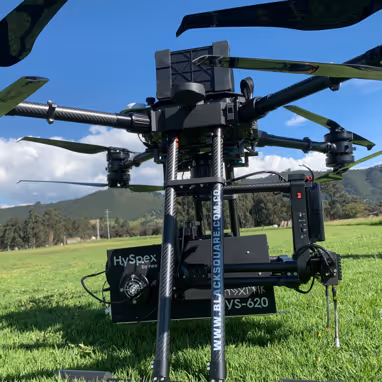 Close-up of a large black drone with four propellers on a grassy field with mountains and a clear blue sky in the background.