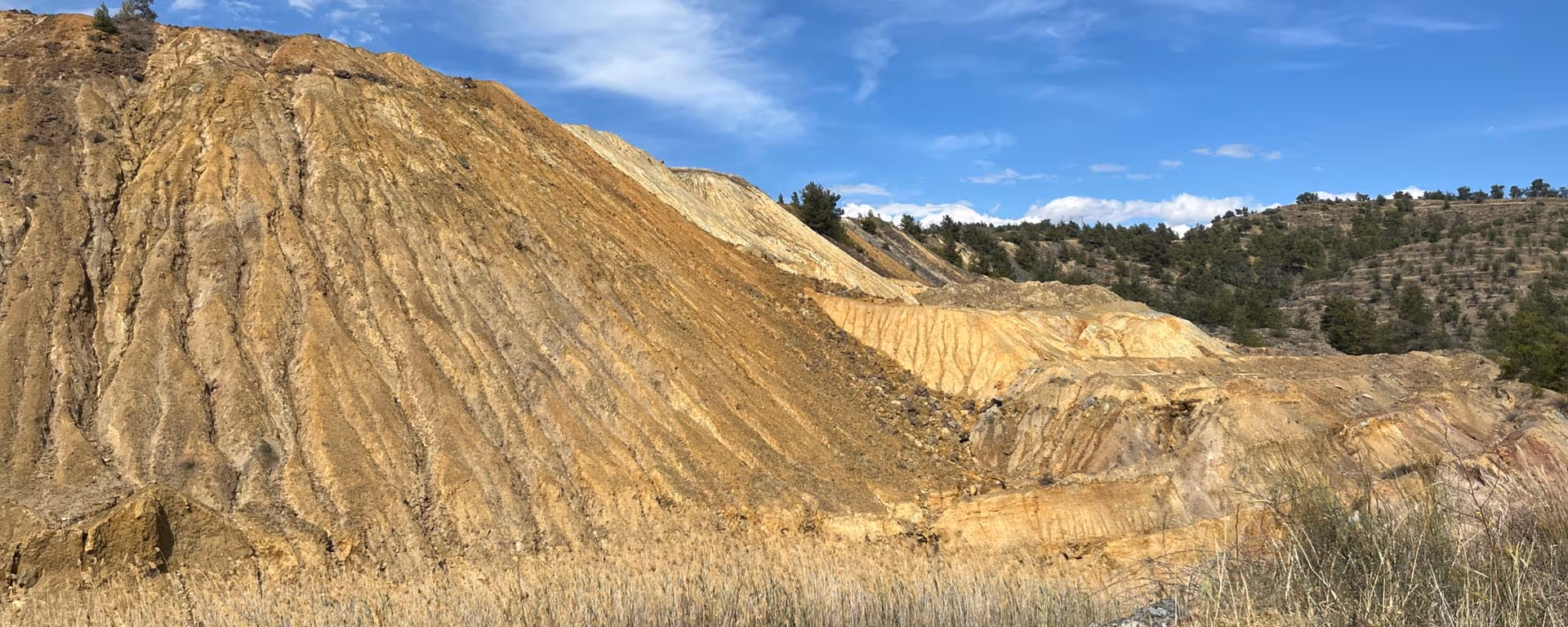 Large exposed hills of layered earth and rock with sparse vegetation under a partly cloudy blue sky.