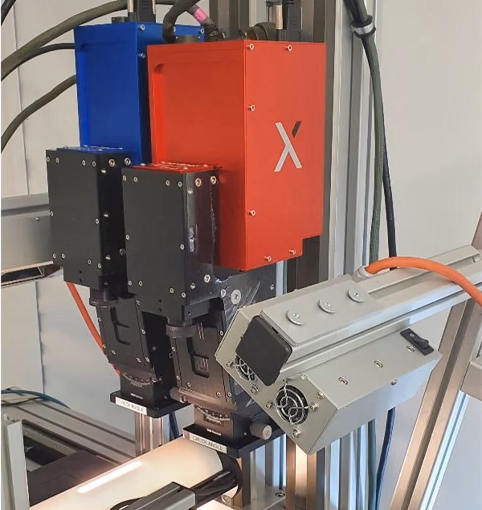 Close-up of an industrial machine with red, blue, and black components, including a red box marked with a white 'X' and attached cables.