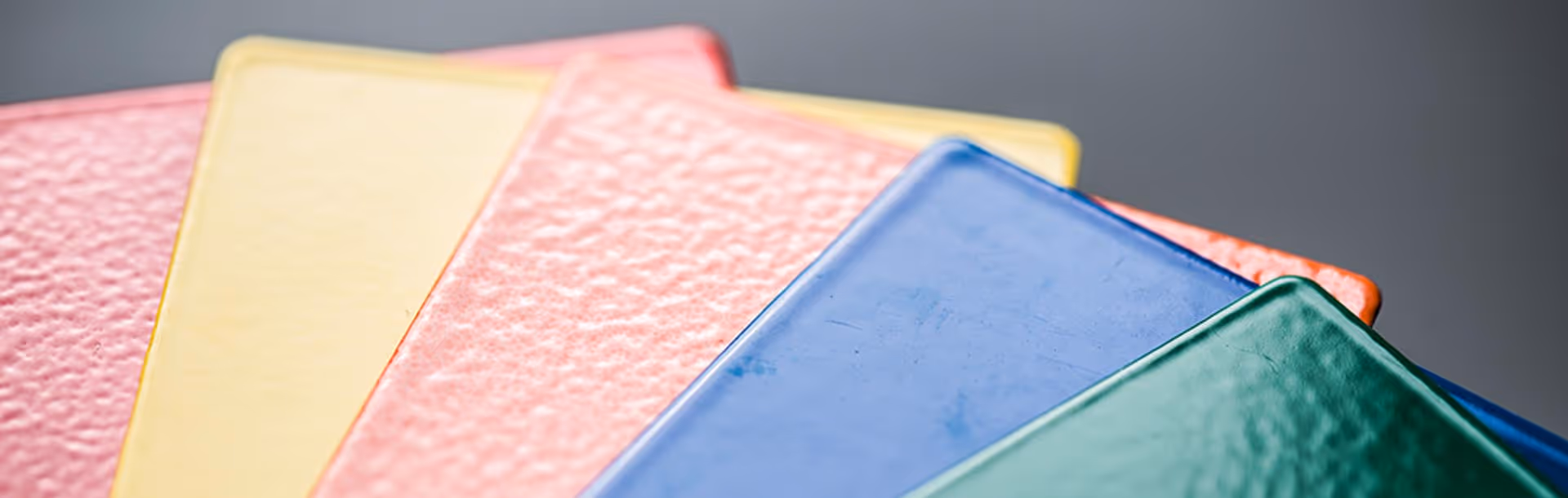 Close-up of five textured rectangular tiles in green, blue, pink, yellow, and red overlapping each other on a gray surface.