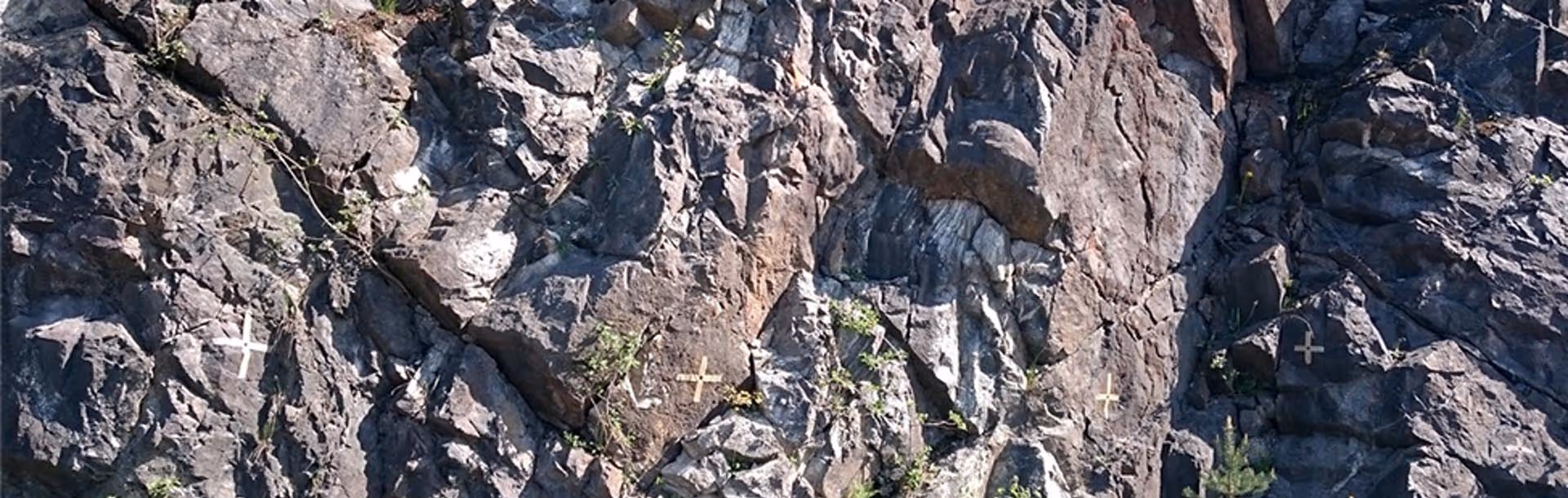 Rocky cliff face with several painted cross marks and sparse vegetation in the crevices.