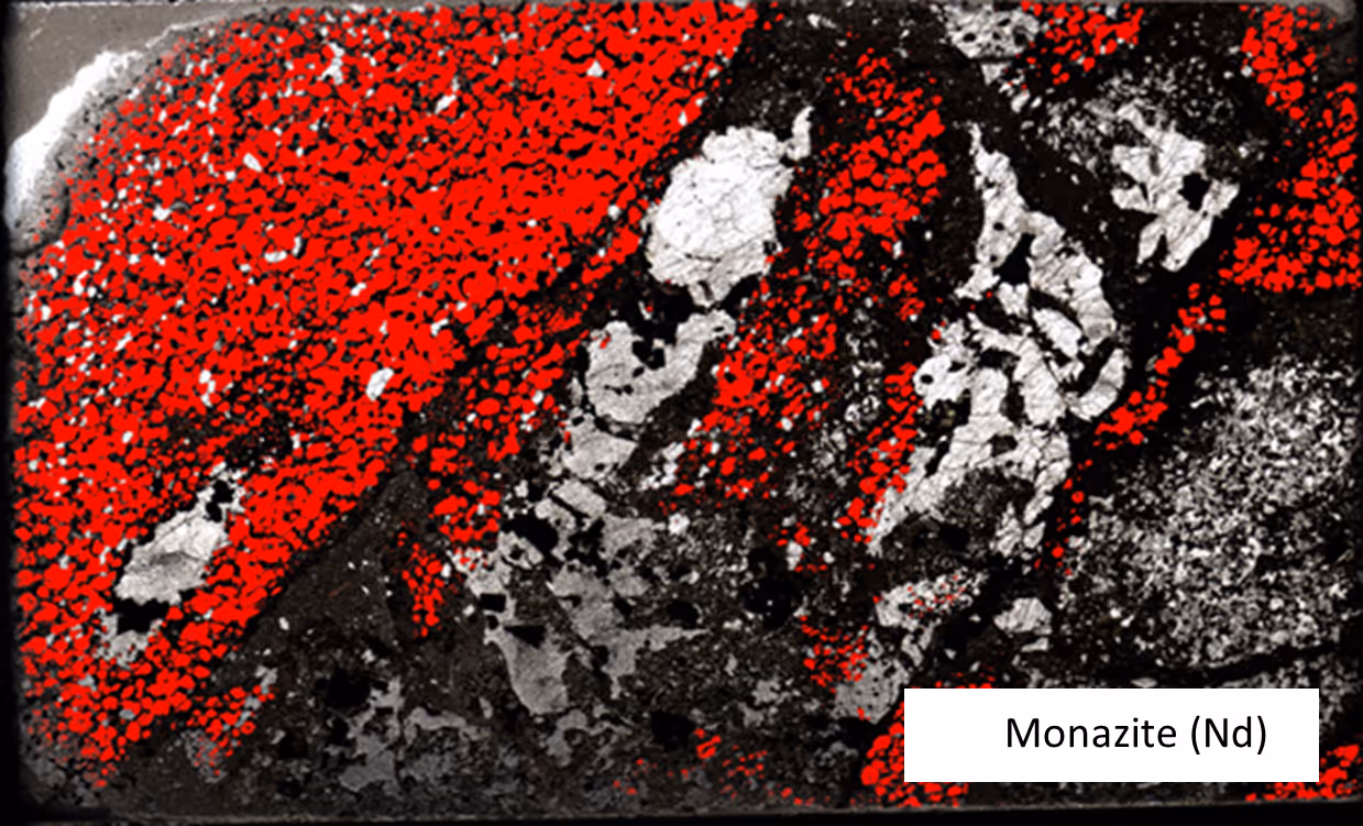 Microscopic image of a rock thin section with red and white mineral grains, labeled Monazite (Nd).