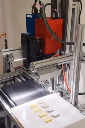 Industrial machine with a red and blue unit mounted on a metal frame, positioned above a surface with small labeled components.