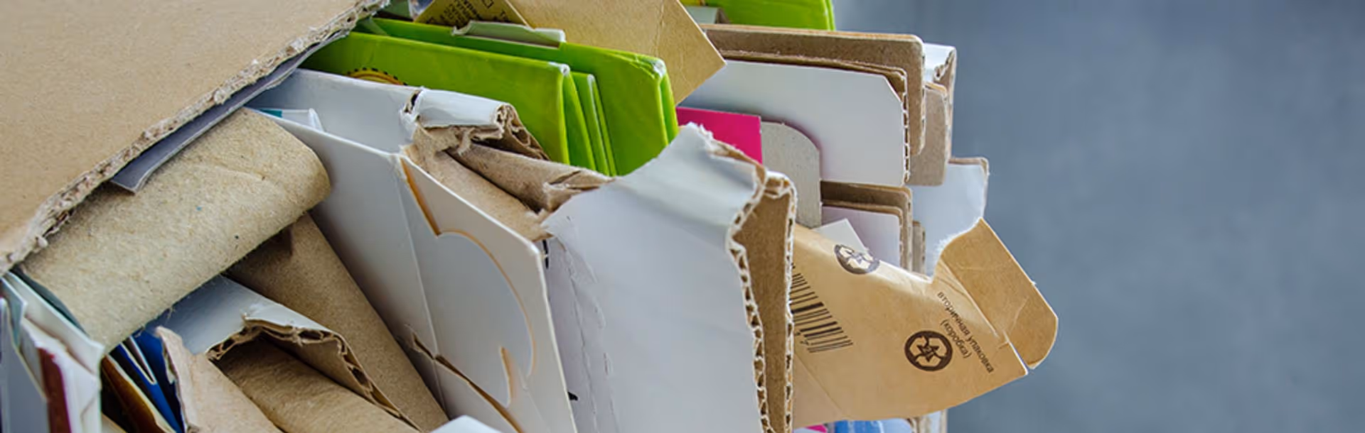 Stack of flattened cardboard and paper packaging with some recycling symbols visible.