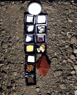 Small samples of soil and rock materials displayed in a vertical line on rocky ground.
