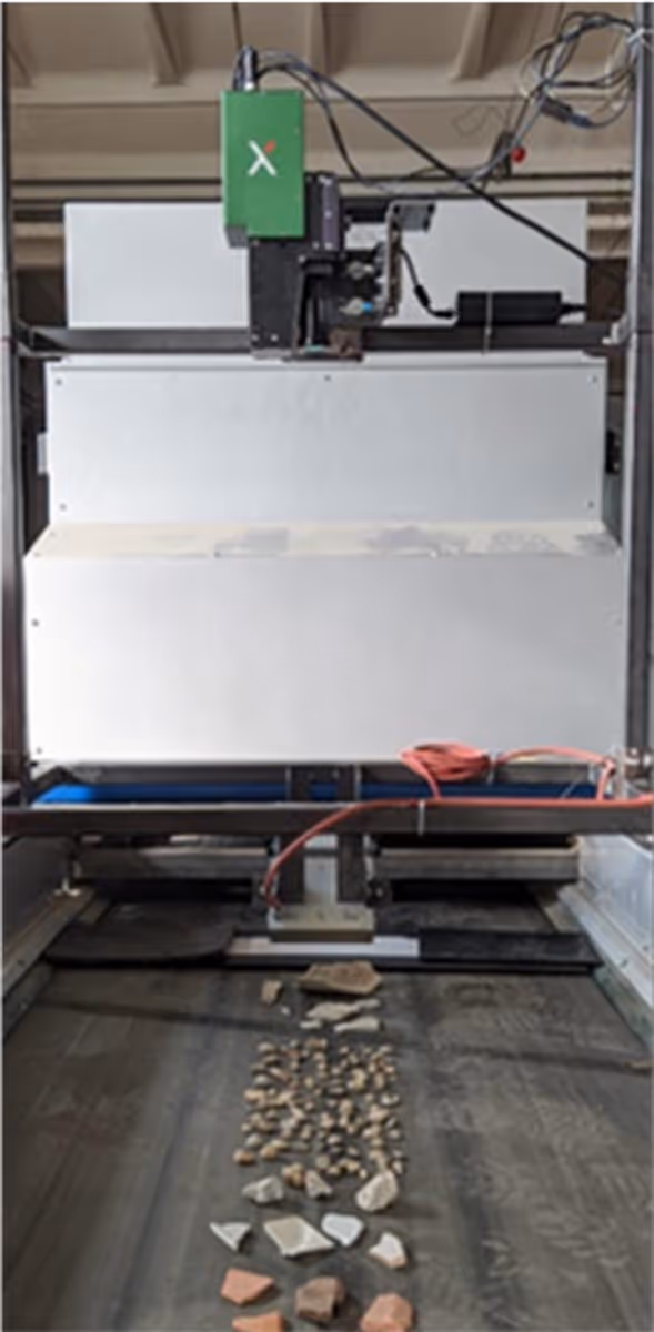 Machine with a green control box sorting various small rocks and stone fragments on a conveyor belt.