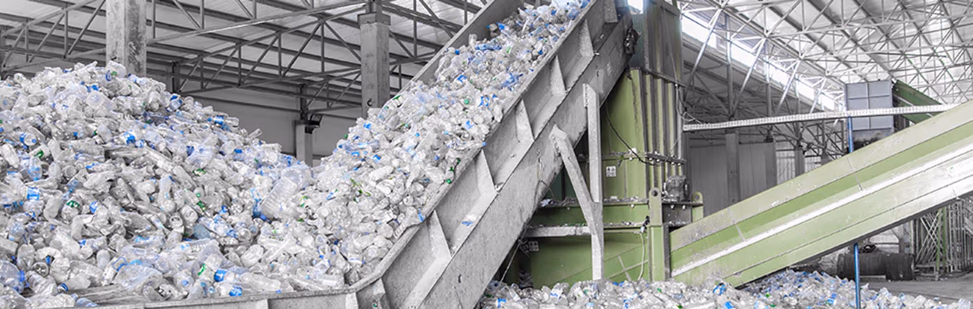 Industrial facility conveyor belts transporting large piles of clear plastic bottles for recycling.