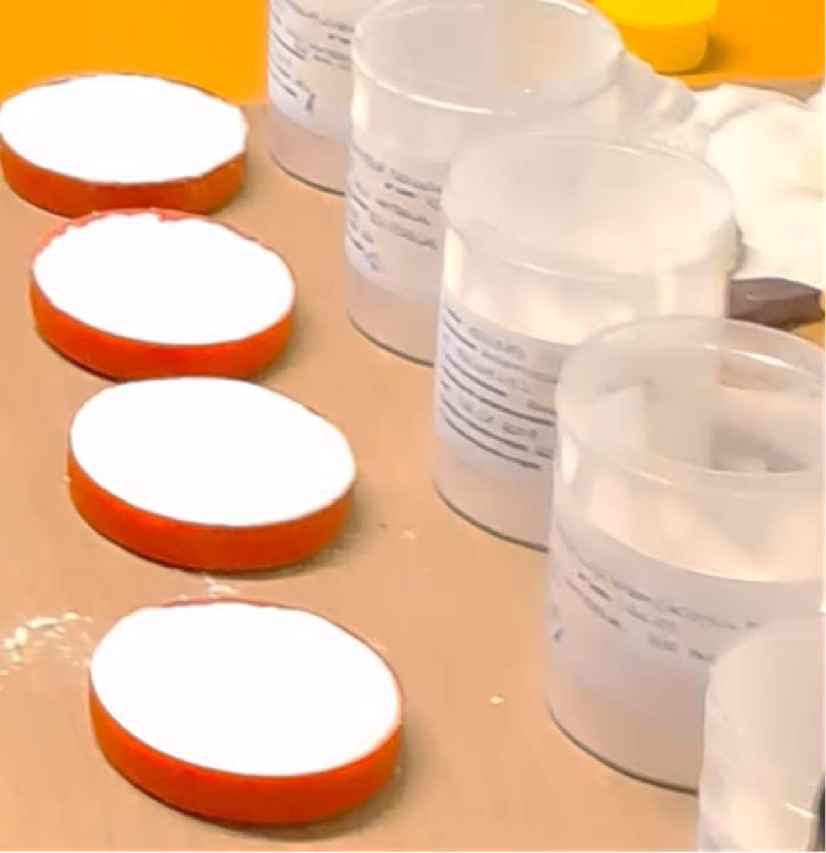 Close-up of open plastic containers with white powder and orange lids placed on a surface.