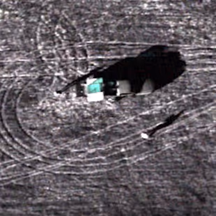 Aerial view of a tractor working on a field with visible tire tracks and a person walking nearby.