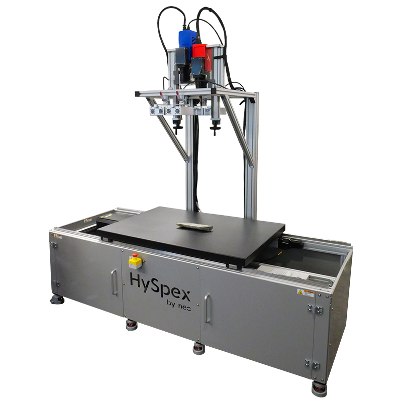 HySpex laboratory scanning rack with metallic frame and black scanning surface featuring a mineral sample. One red HySpex hyperspectral camera and one blue HySpex hyperspectral camera hang above the scanning surface