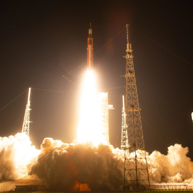 Rocket launching at night with bright flames and smoke billowing around the launch pad.