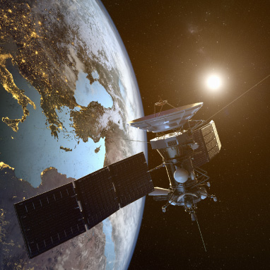 Satellite with solar panels orbiting Earth with the sun shining brightly in the background.