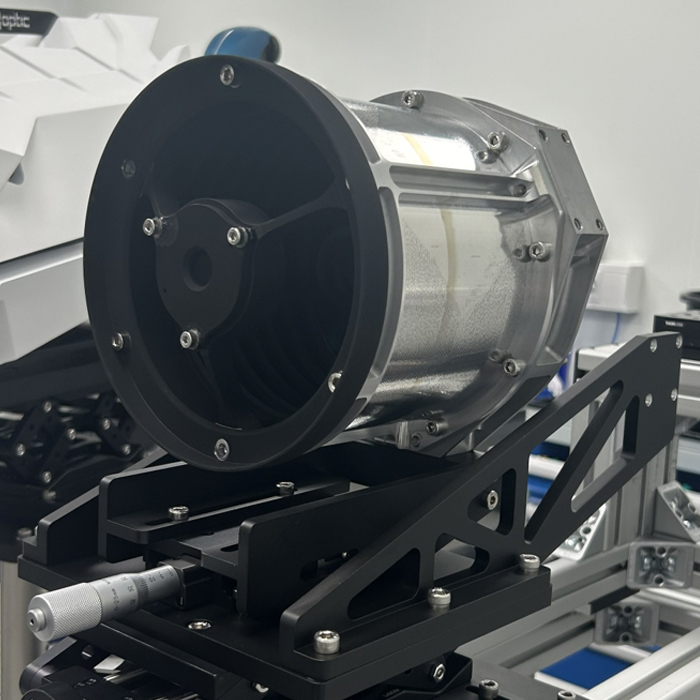 Close-up of a metallic cylindrical device mounted on a black adjustable frame in a lab.