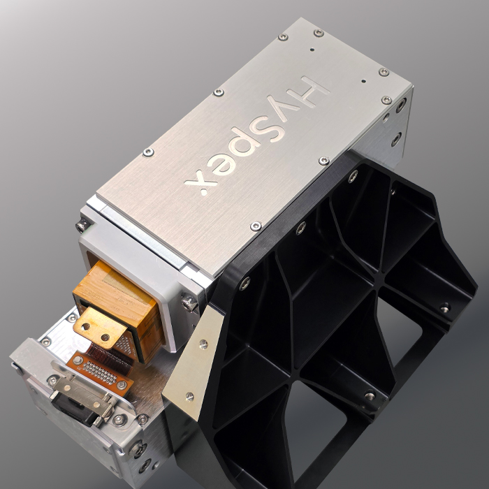 Close-up of a HySpex hyperspectral imaging sensor created for use in the stratosphere, with metallic and black components on a gray gradient background.