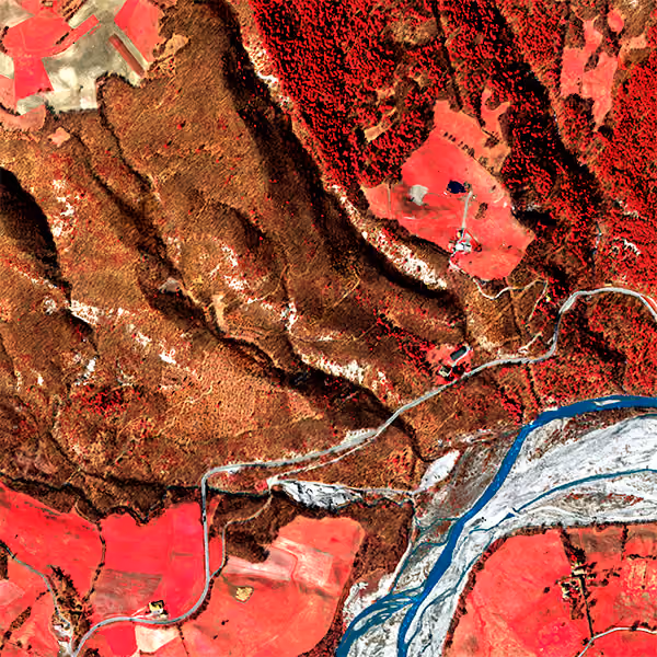 Aerial view of a landscape with red agricultural fields, brown forested hills, and a winding blue river running through the bottom right.
