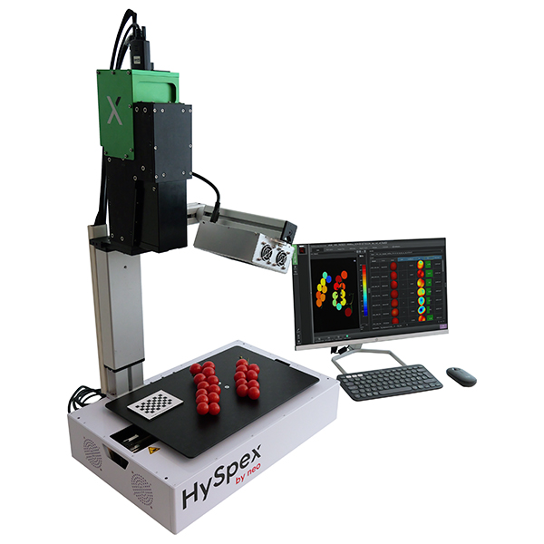 A tabletop scanning workstation, including a green hyperspectral camera, lamps for illumination, a scanning stage on a white box and a PC with data analysis software and a mouse and keyboard attached