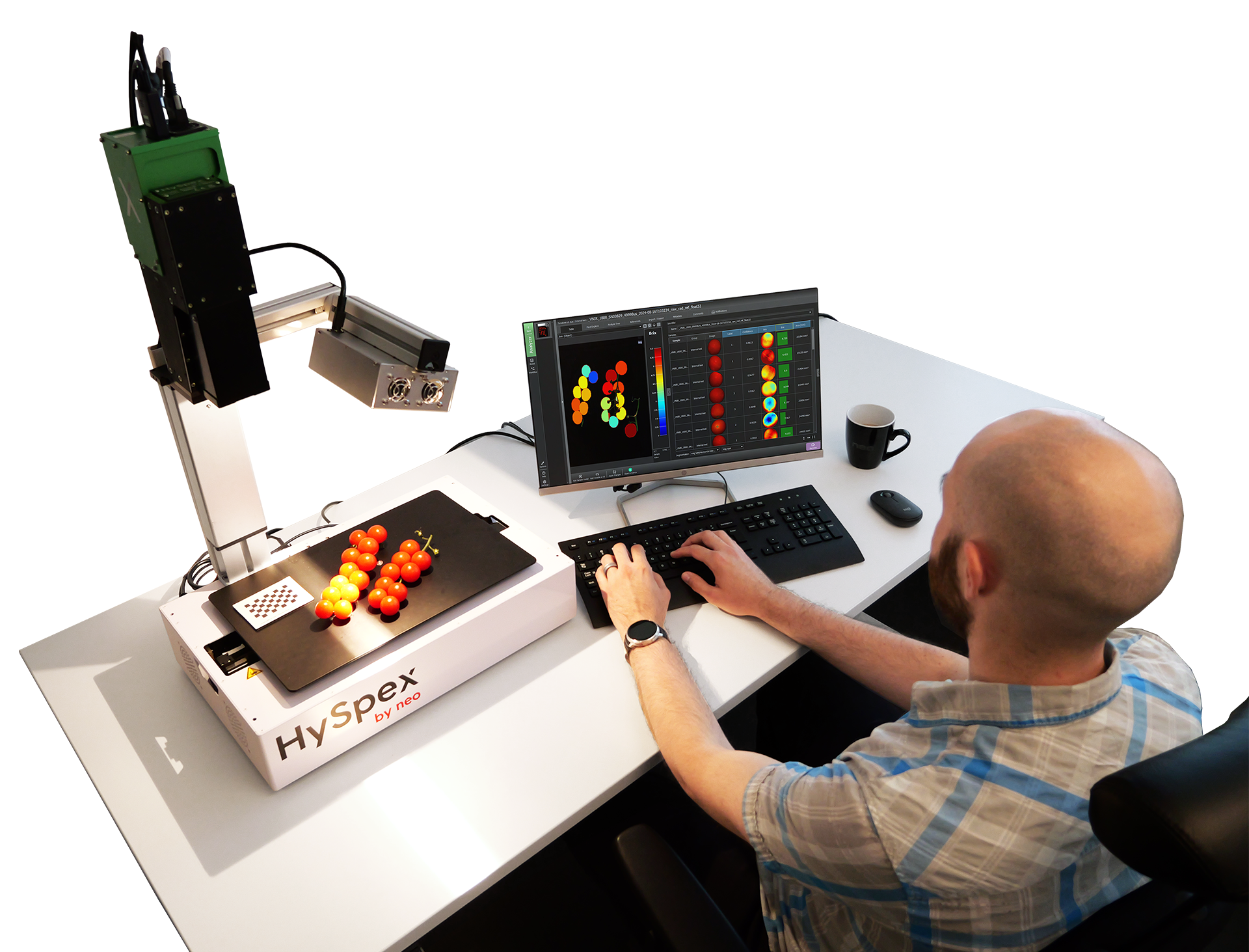 Man uses HySpex tabletop workstation to scan cherry tomatoes arranged on a tray, analyzing data on a computer screen.