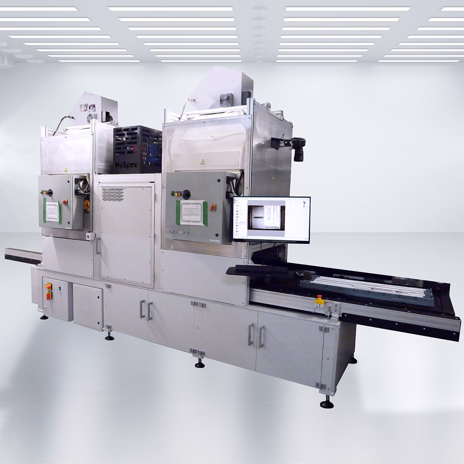 Large industrial Core Scanner machine with a conveyor belt, control panels, and a mounted monitor displaying scanning data in a bright, clean white room with a grid of ceiling lights.