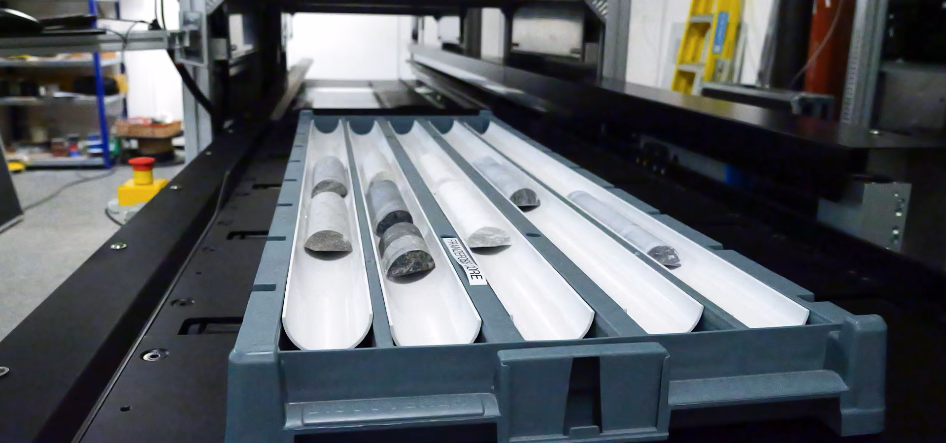 Tray holding five cylindrical rock core samples in a scanning machine within a lab or industrial setting.