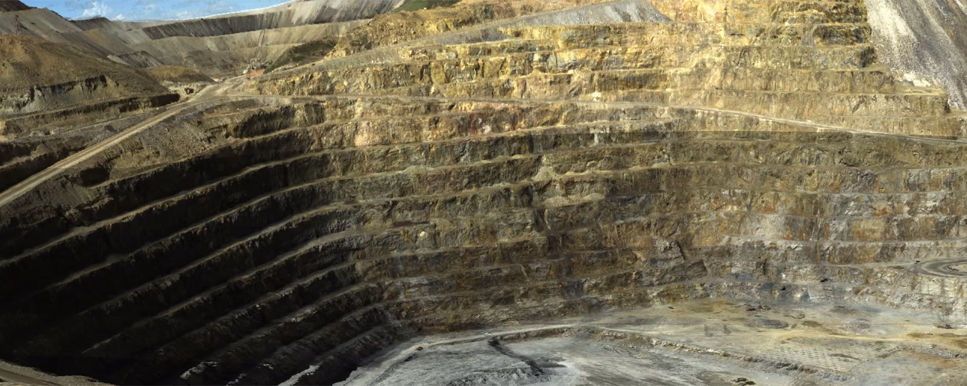 Wide view of a deep stepped open pit mine with terraced layers of earth exposed and clear blue sky above.