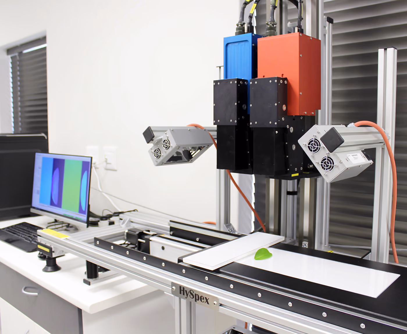 A hyperspectral camera laboratory setup with a scanning stage and a connected computer on the left