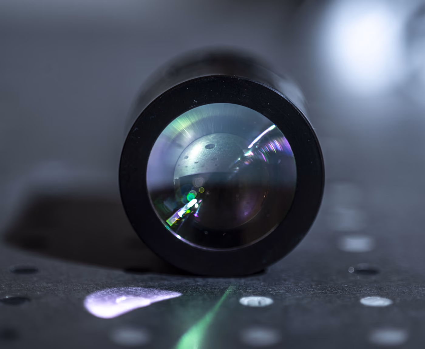 A shiny lens, reflecting colors and light onto a metallic surface with small holes in it