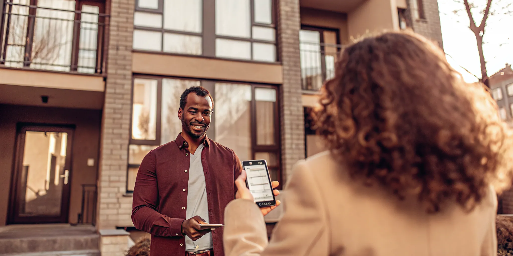A renter holding a smartphone showing a credit score and a reusable tenant screening report with an apartment building in the background