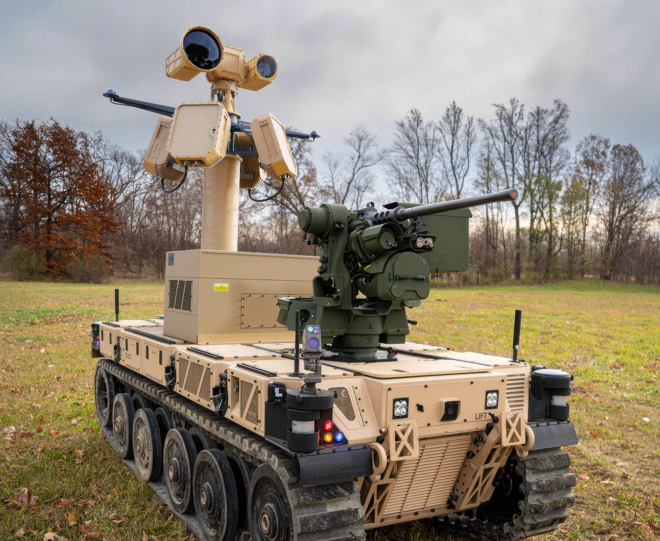Beige military unmanned ground vehicle with mounted EchoShield sensors on a grassy field with trees in the background.