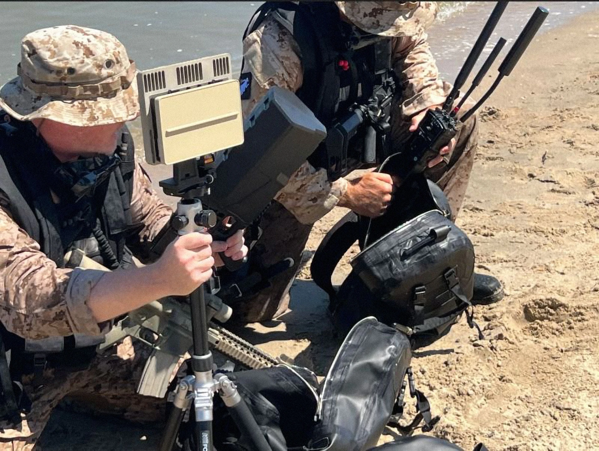 Two soldiers in camouflage uniforms on a sandy beach handling EchoGuard radars