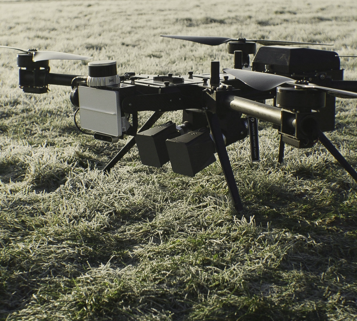 Close-up of a black quadcopter drone with attached EchoShield sensors and cameras standing on frosty grass.