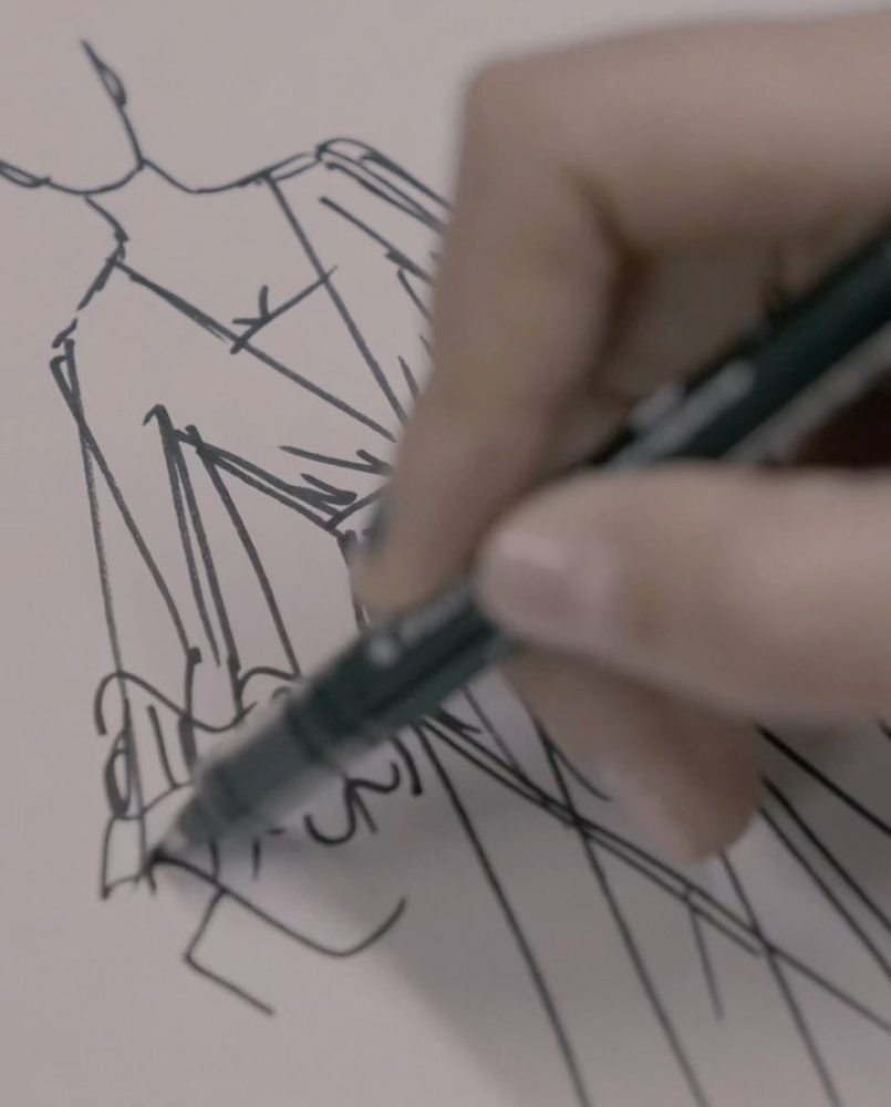 Main dessinant une esquisse de mode d'une silhouette vêtue d'une robe élégante à l'aide d'un stylo noir.