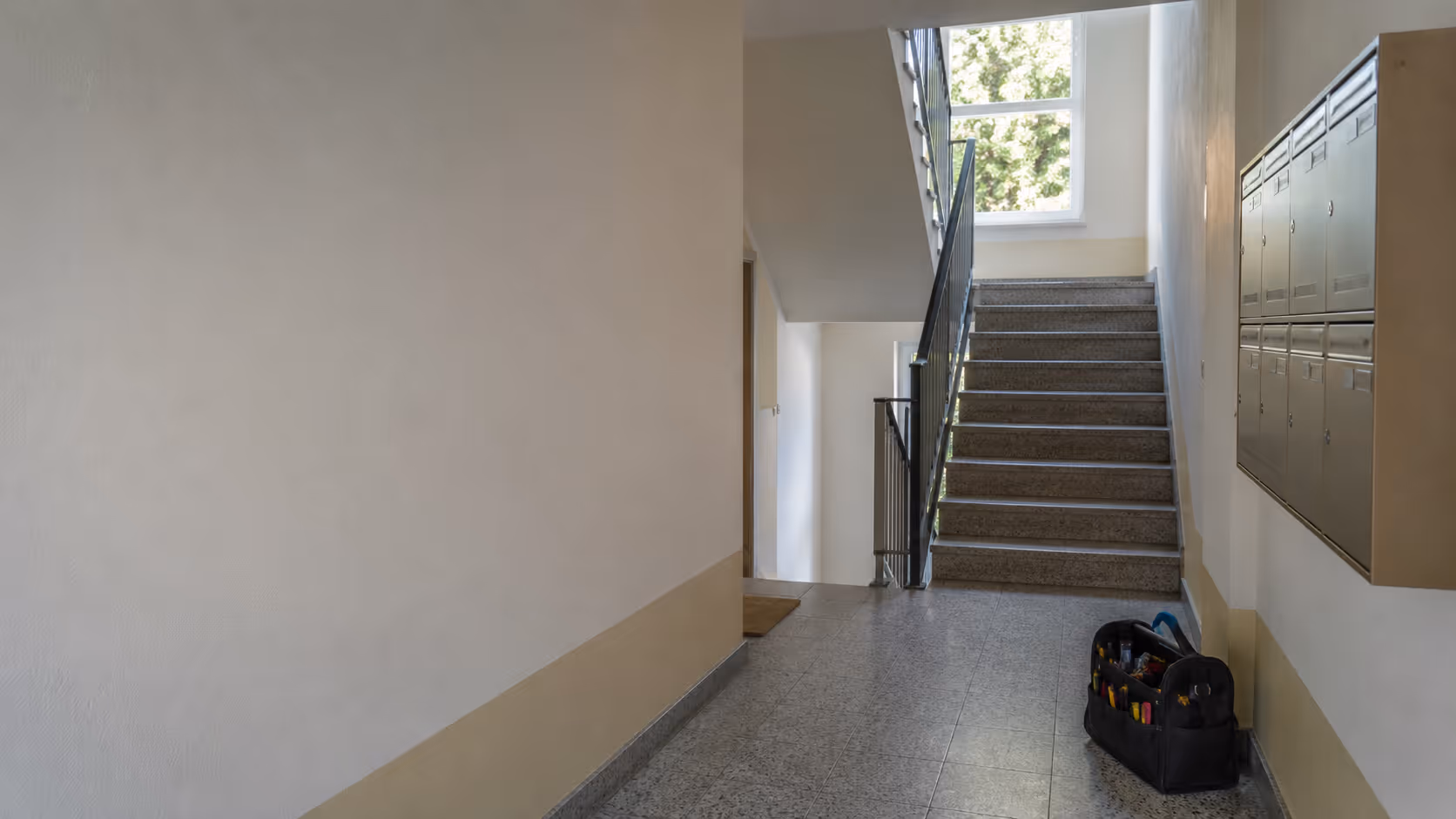 Sauberes Treppenhaus mit Werkzeugtasche in einem Mehrfamilienhaus als Symbol für Hausmeisterservice und Gebäudebetreuung.