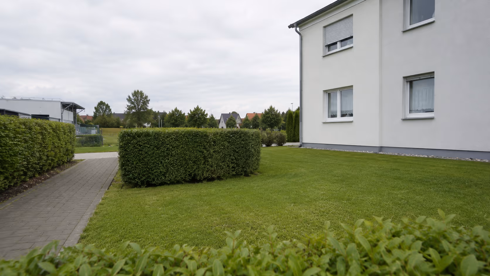 Gepflegte Grünfläche mit Hecken und Pflasterweg vor einem Gebäude als Beispiel für Grünpflege im Wetteraukreis.
