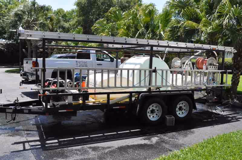 Technician performing safe roof cleaning service on two-story home removing years of algae buildup