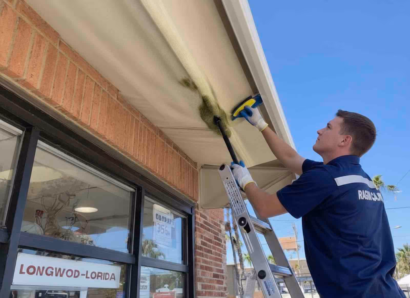 Awning cleaning crew restoring faded canvas color and removing algae buildup at commercial storefront
