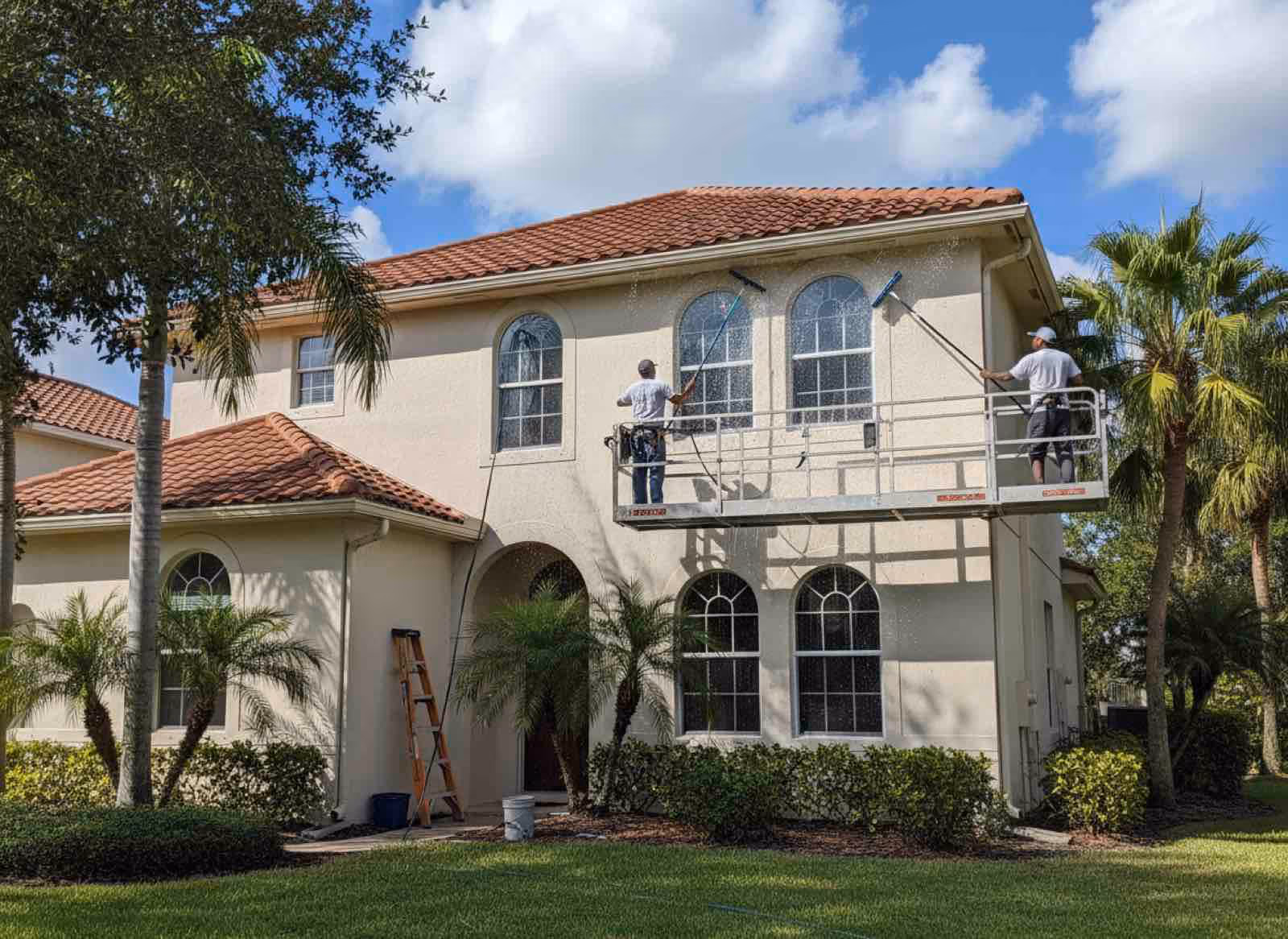 Technician performing exterior window cleaning using water-fed pole system to reach upper story windows