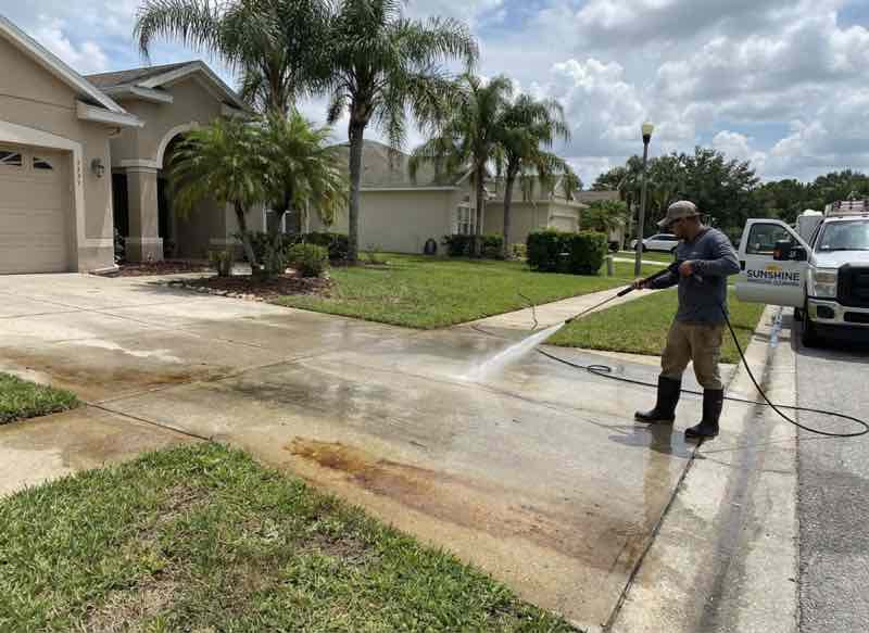 Professional pressure washing service cleaning residential garage door and driveway in Longwood FL with palm trees and two-story home