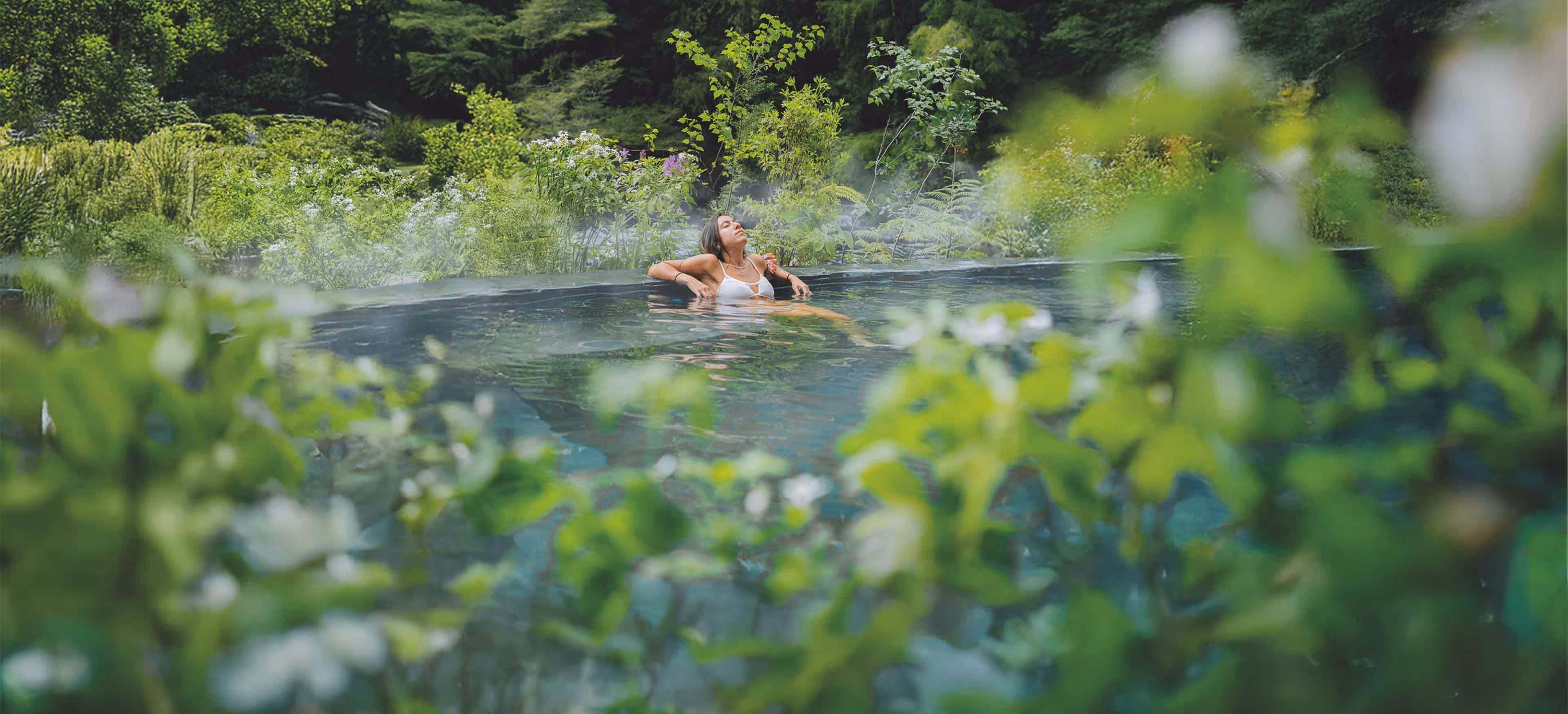 Mujer inmersa en naturaleza bañándose relajada en las piscinas termales