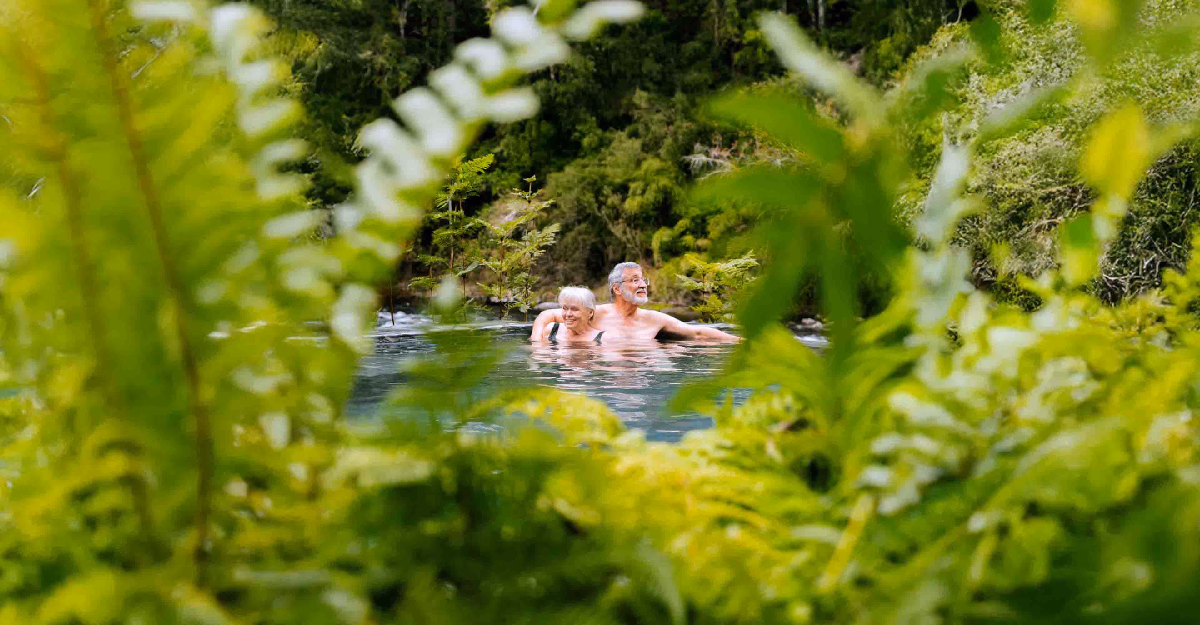 Dos adultos mayores disfrutando de las aguas termales rodeados de naturaleza nativa