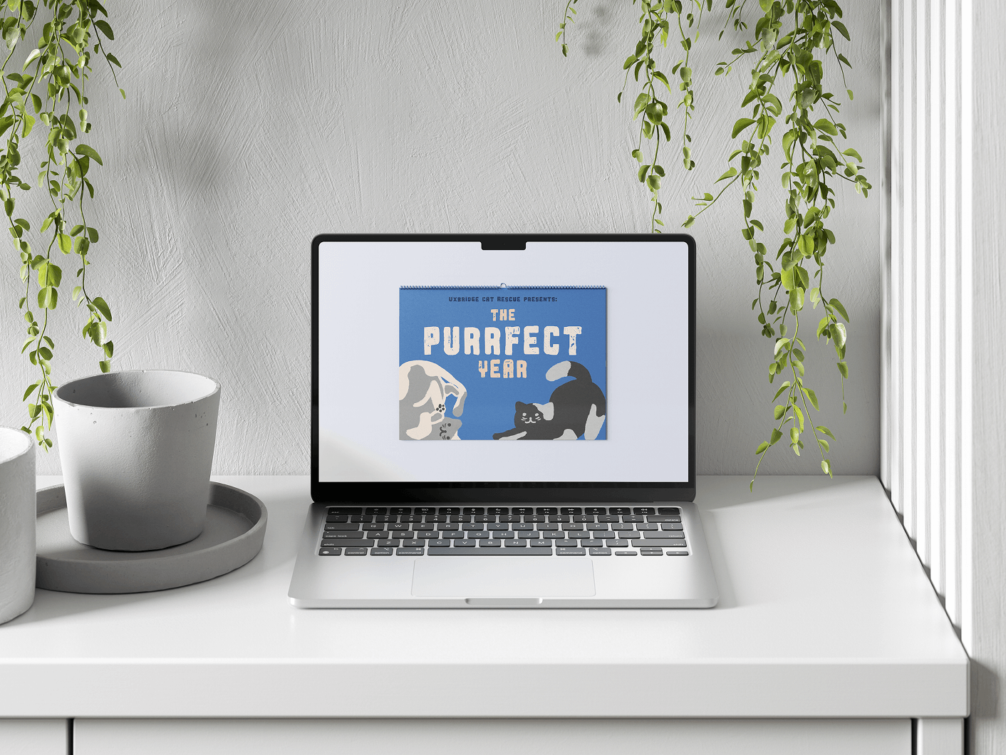 Open laptop on white desk displaying a blue calendar page titled 'The Purrfect Year' with illustrations of two stretching cats.