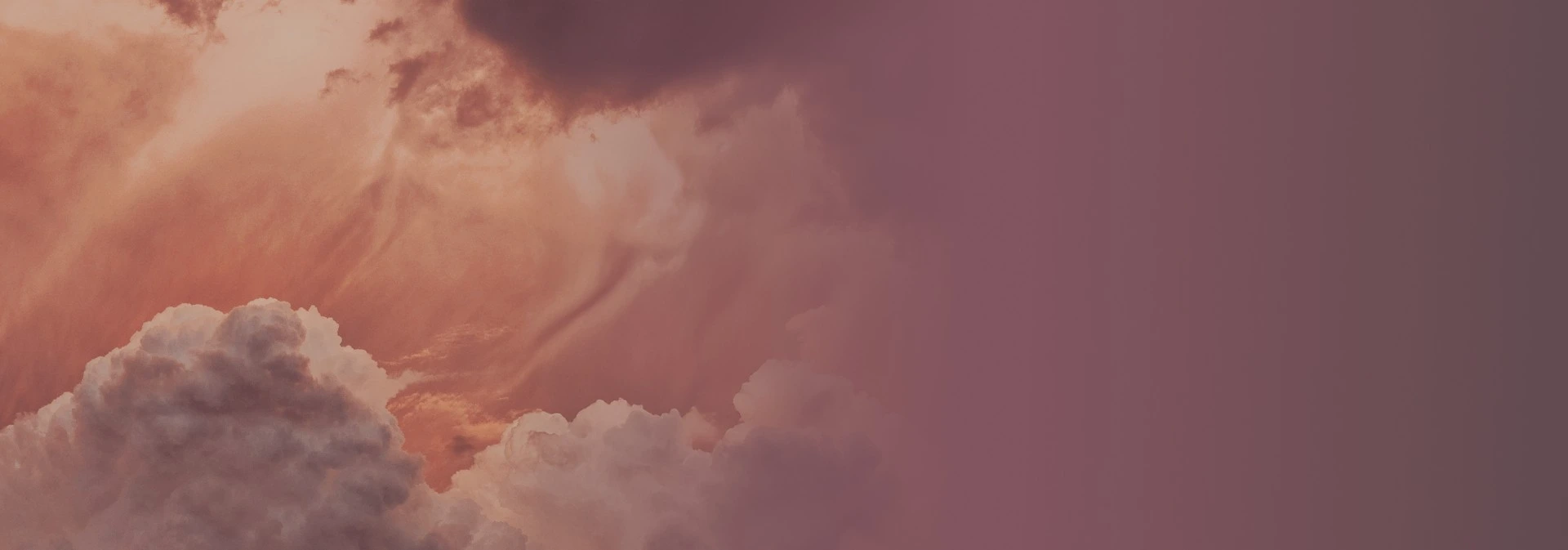 Clouds at sunset with an orange and pink sky fading into a purple gradient.