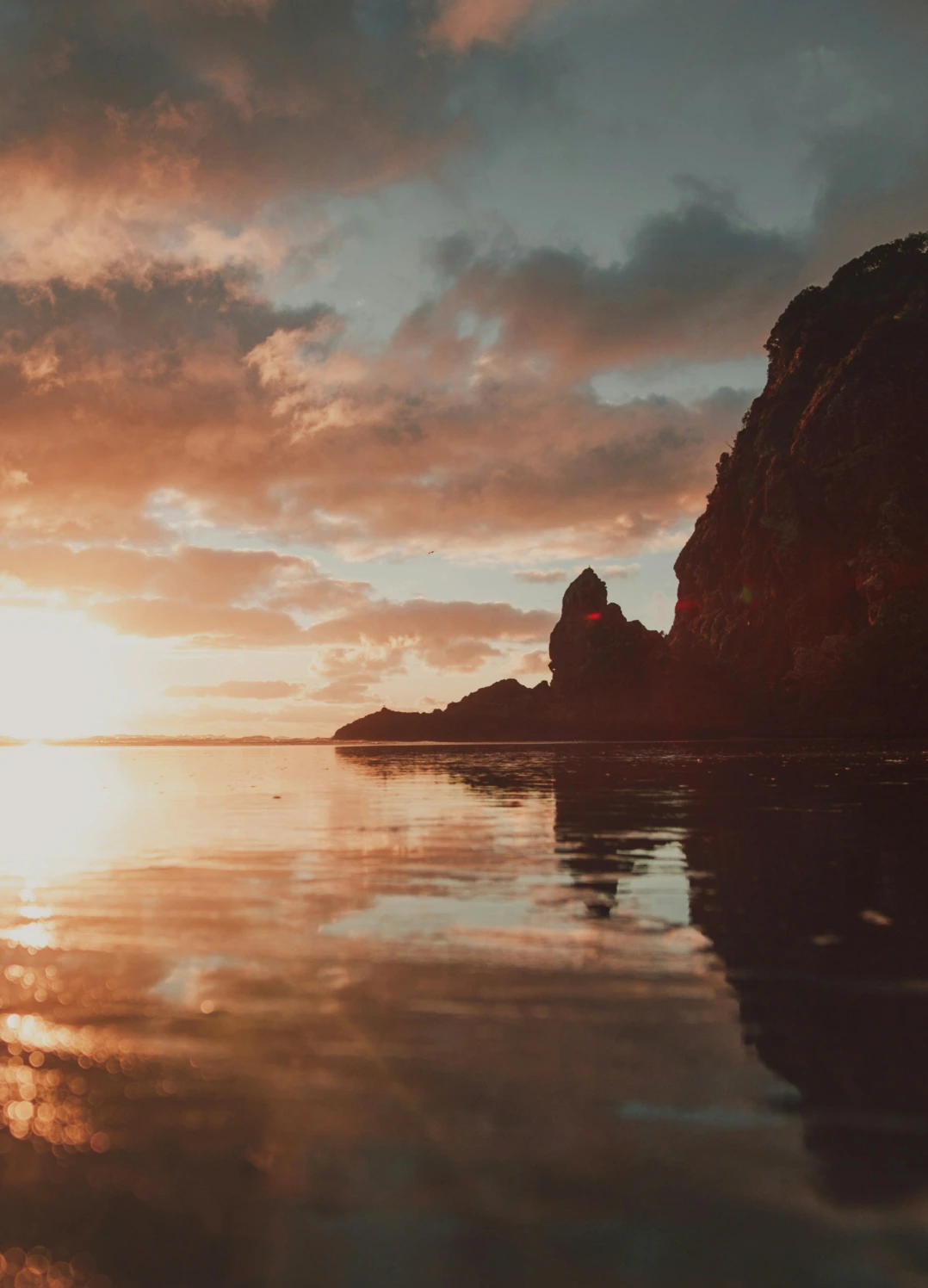 Sunset casting an orange glow over calm waters with rocky cliffs silhouetted on the right.