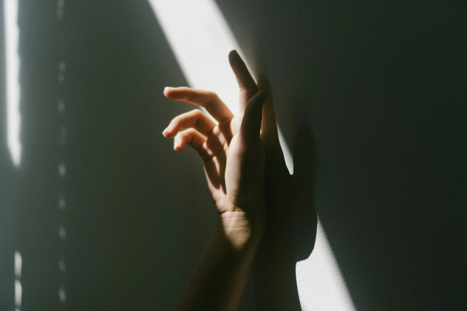 Hand reaching towards a wall with light and shadow creating contrast across the fingers and surface.