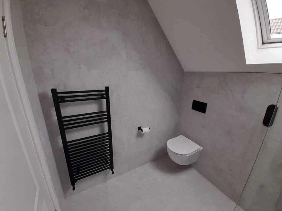 Minimalist bathroom corner with wall-mounted toilet, black towel radiator, and a skylight window.