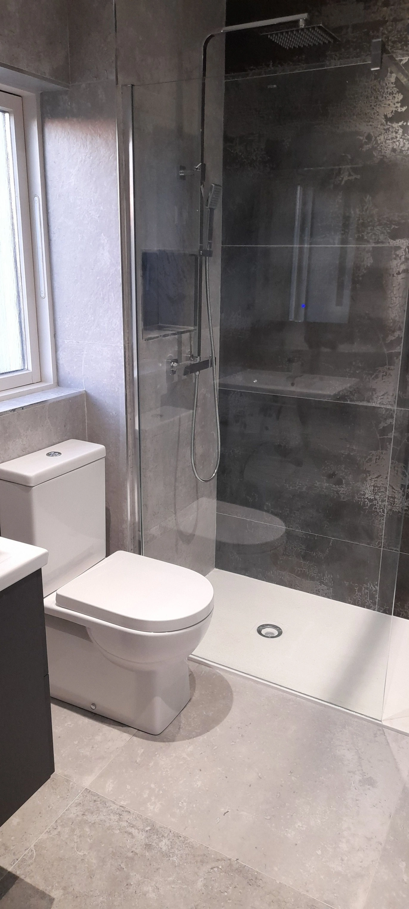Modern bathroom with white toilet next to a walk-in shower with glass door and dark tiled wall.